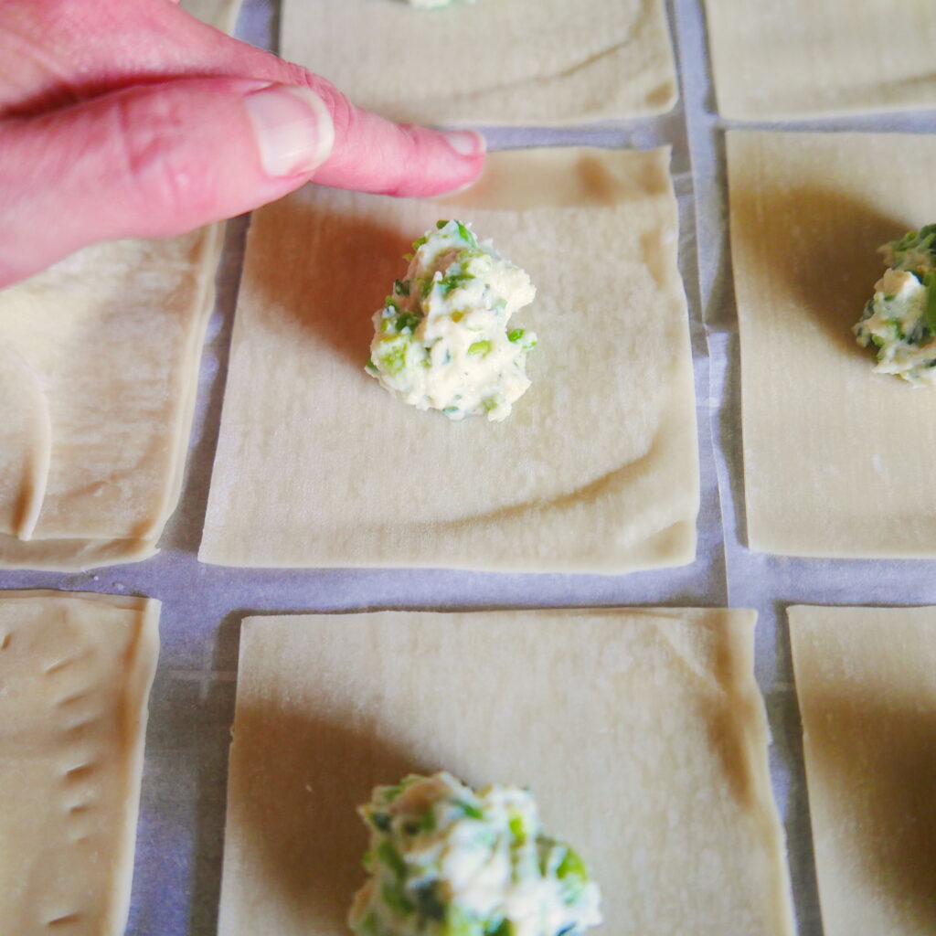 white hand wetting a wonton wrapper that is being assembled to make vegetarian pea ravioli