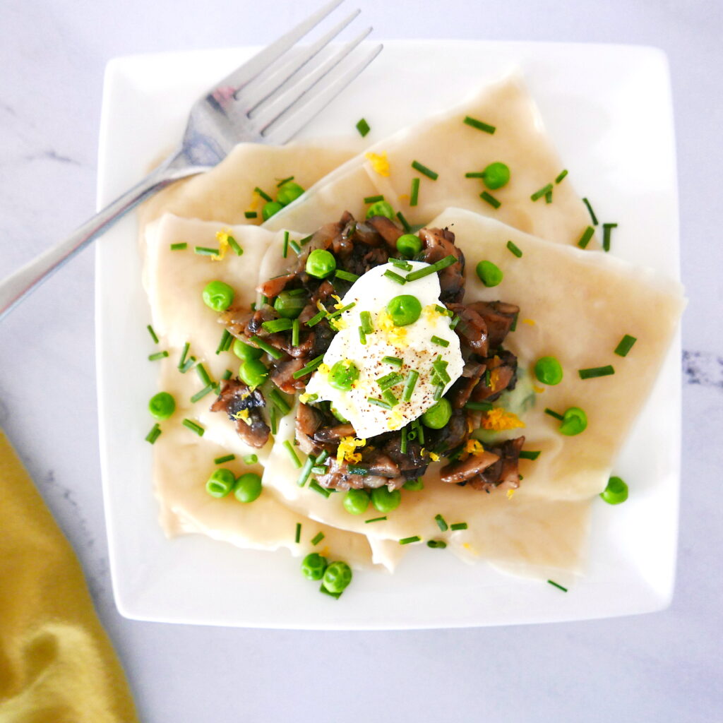 ricotta pea ravioli with mushrooms assembled on a white plate with fork and a green napkin next to plate