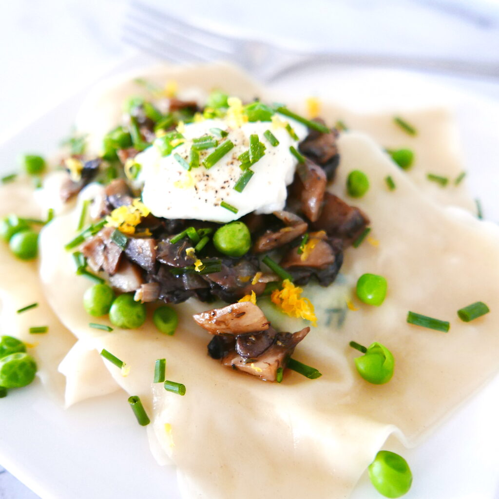 ricotta pea ravioli with mushrooms assembled on a white plate with fork