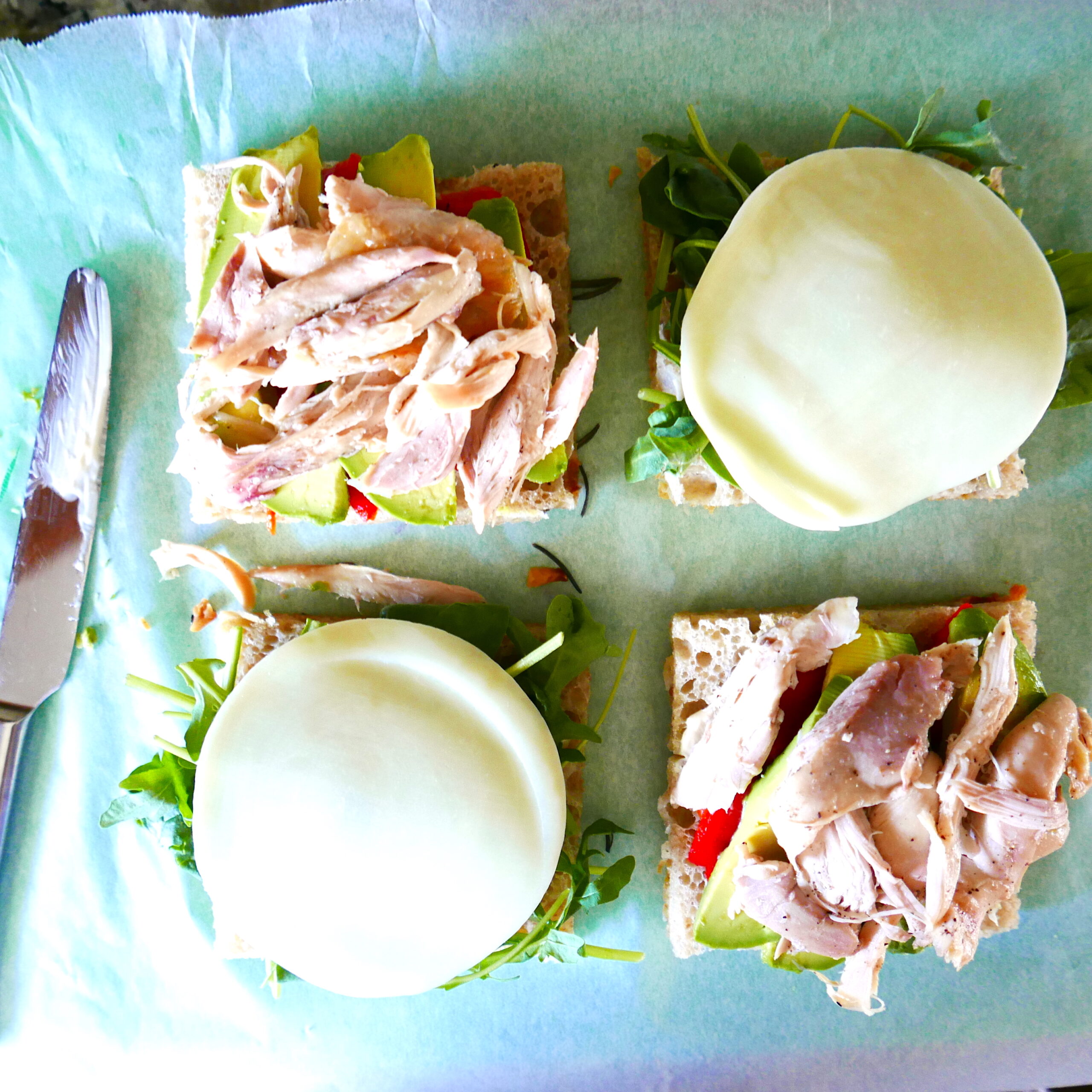 two chicken focaccia sandwiches being assembled on a green cutting board.