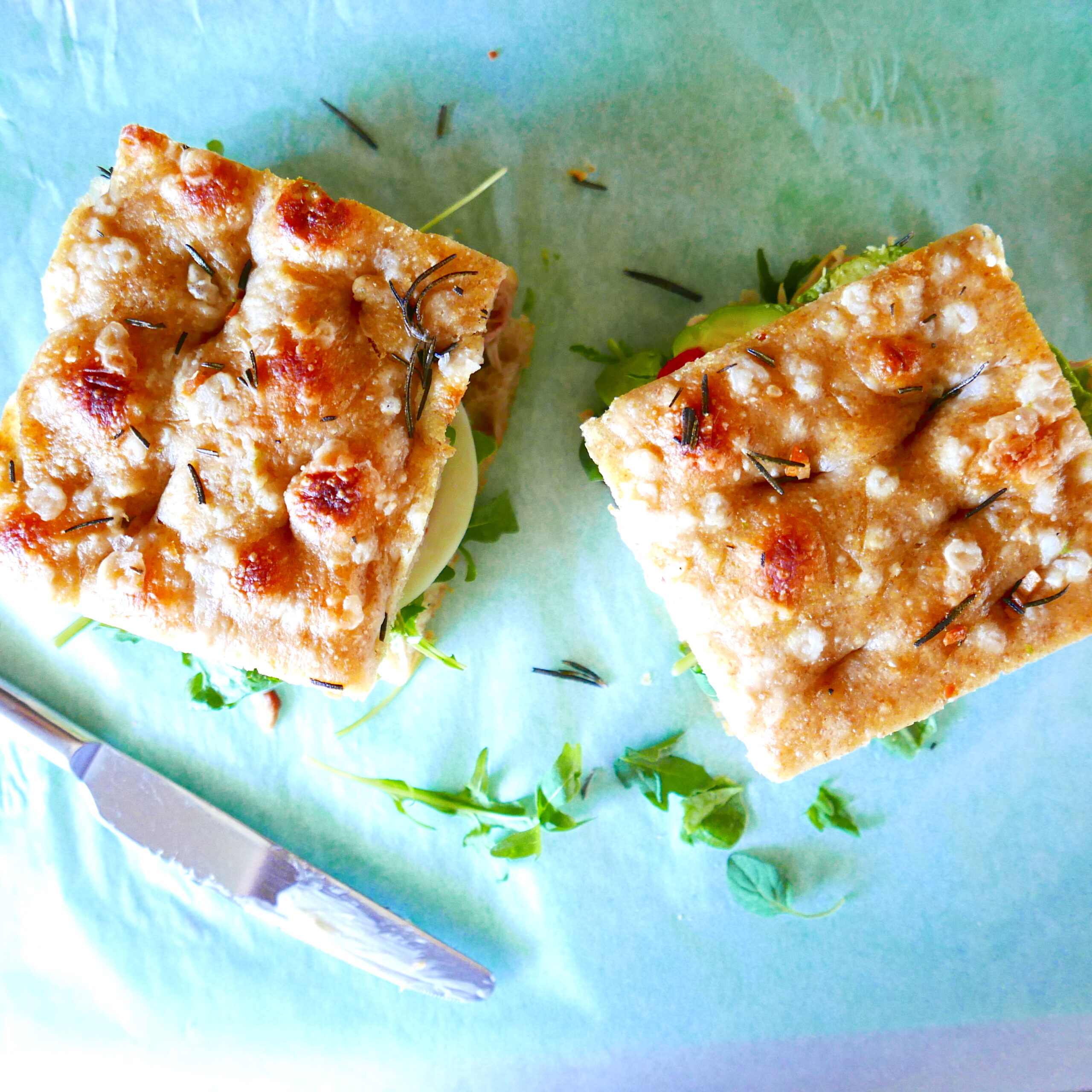 Two sandwiches topped with focaccia on a cutting board. 