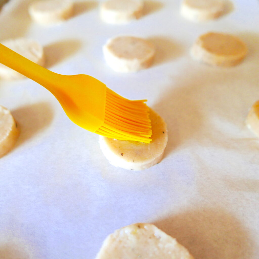 shortbread cookies on a baking sheet with a pastry brush brushing egg white on top