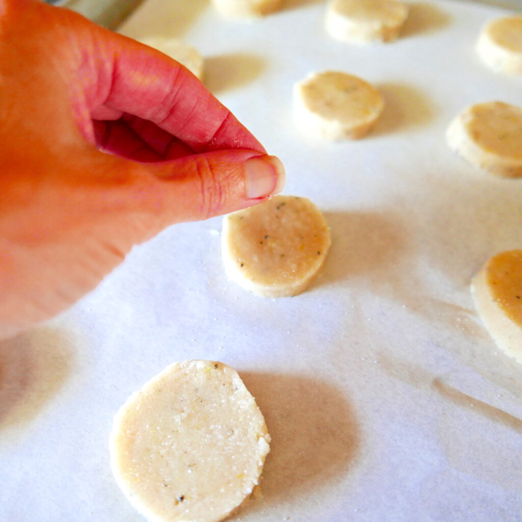 white hand sprinkling sugar onto shortbread cookies on a baking sheet