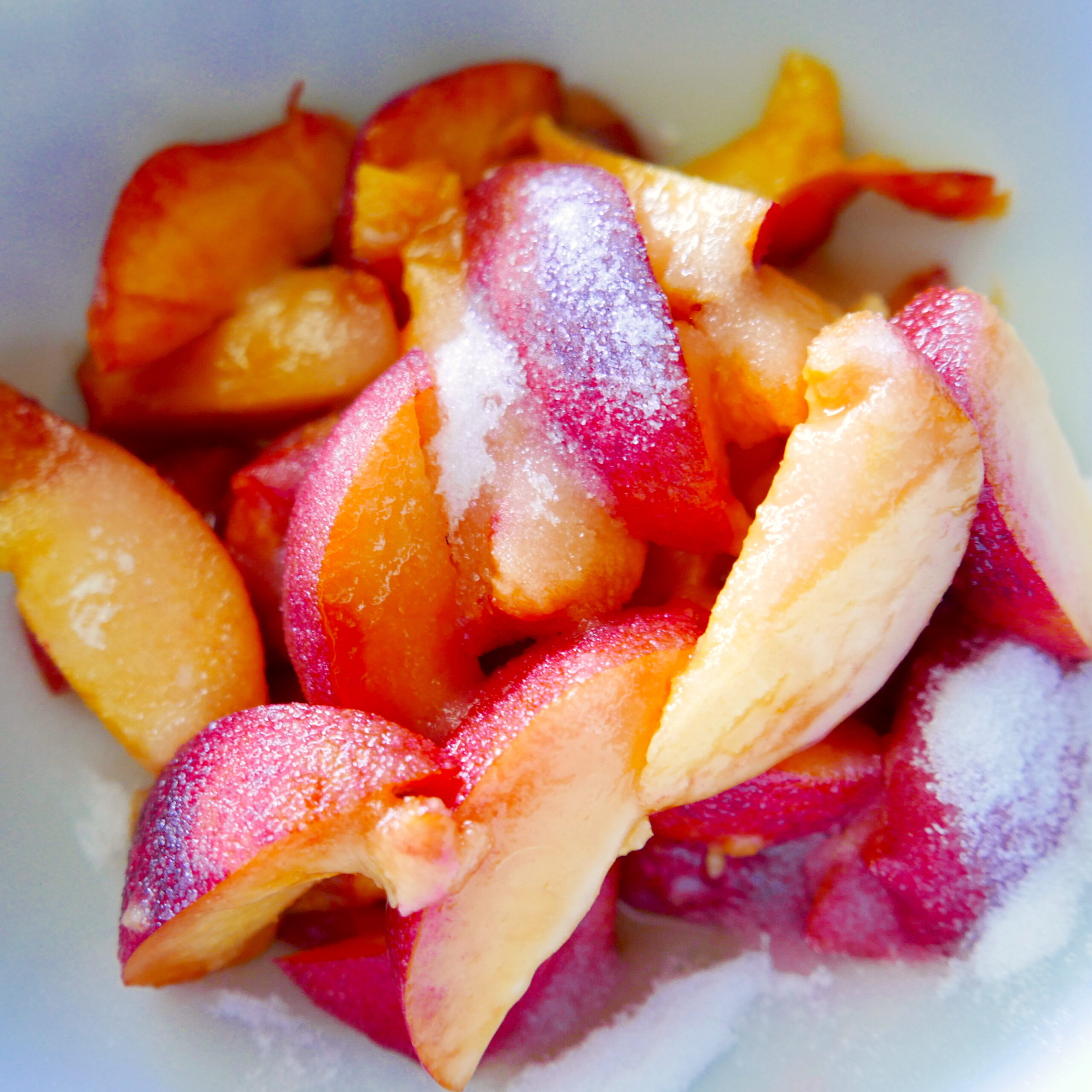 Sliced peaches tossed with sugar and lemon juice in a bowl.
