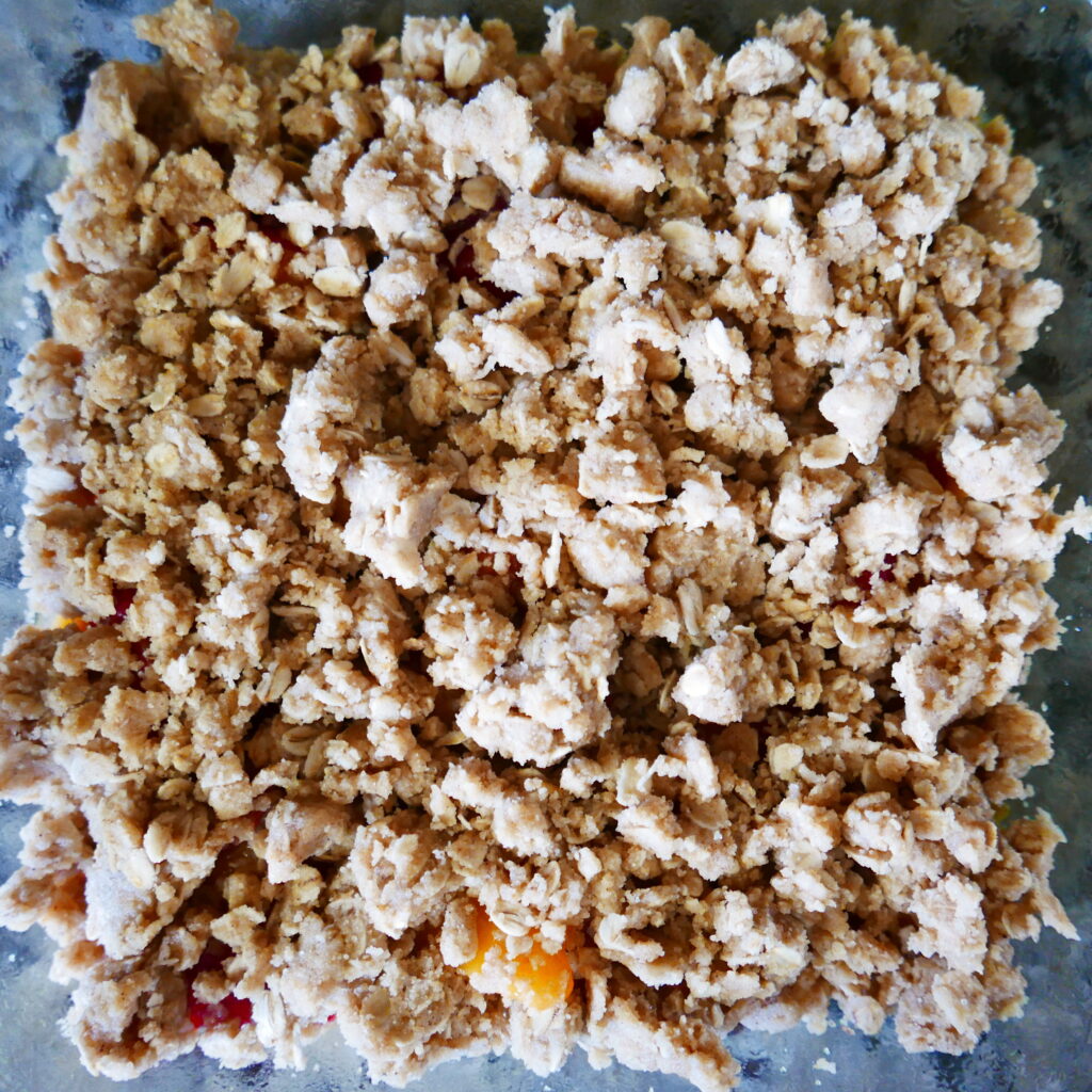 brown butter crumble on top of peaches in a glass baking dish