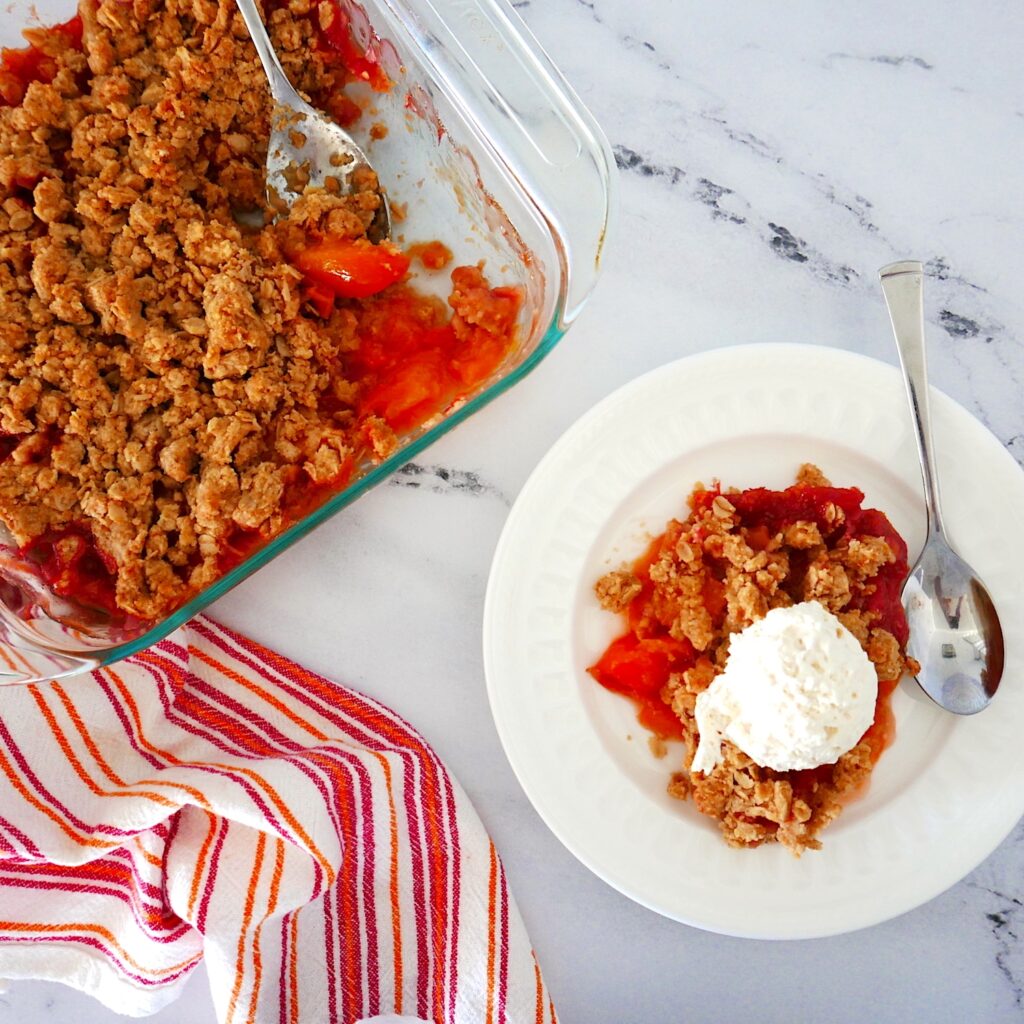 peach crisp with brown butter crumble in a glass pan and on a small white plate with whipped cream and spoon