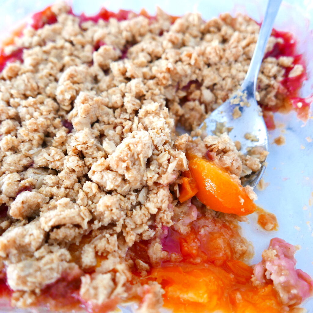 peach crisp in a baking dish with a spoon digging into crisp