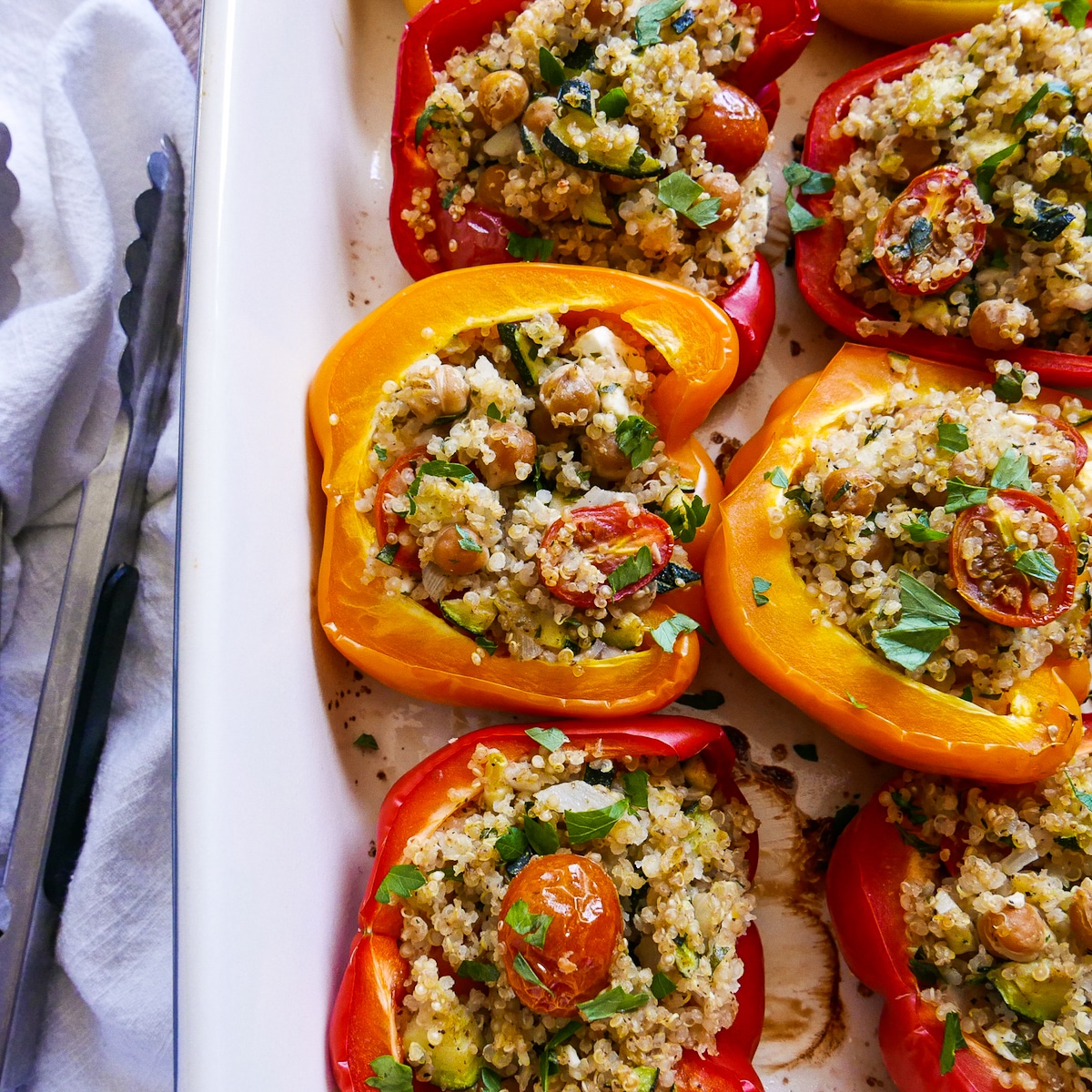 mediterranean stuffed peppers in a baking dish with tongs.