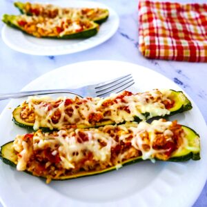 two rice stuffed zucchini boats with fork on a white plate with plaid napkin in background