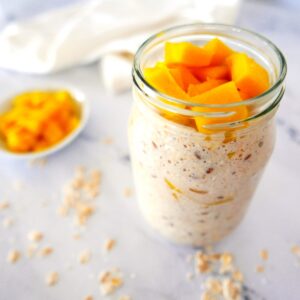 mango overnight oats in a glass jar with cup of mango in background