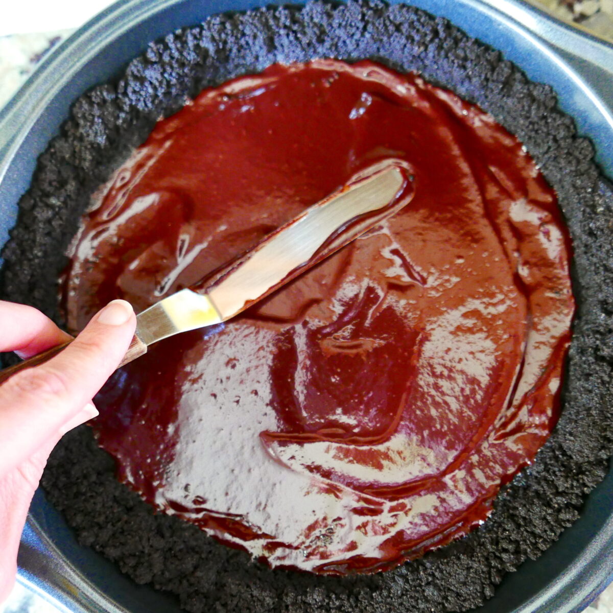 White hand spreading chocolate ganache onto cookie crust.