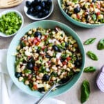 bowl of tuscan bean salad with a spoon, fresh basil, and a napkin.