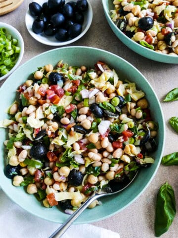 bowl of tuscan bean salad with a spoon, fresh basil, and a napkin.