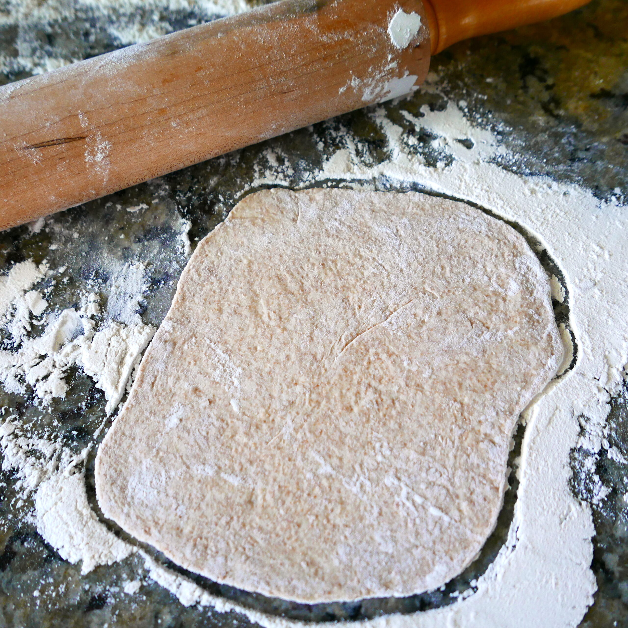 sourdough naan being rolled out on a counter with rolling pin.