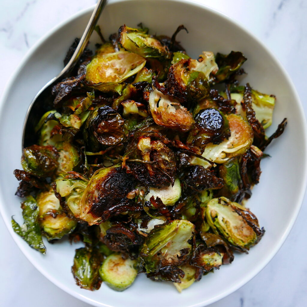 roasted brussel sprouts in a large white bowl with serving spoon