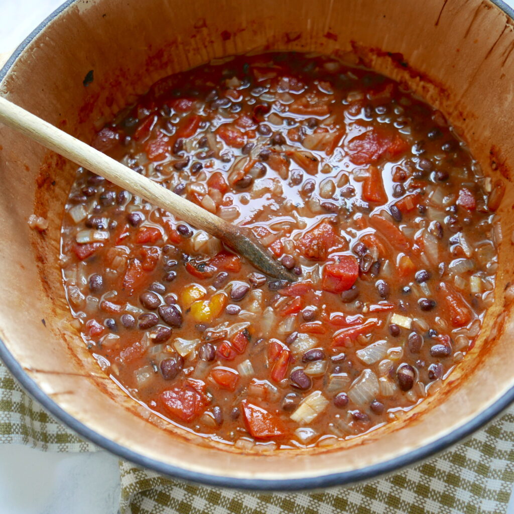 tomatoes, black beans, and onions being cooked in a large pot