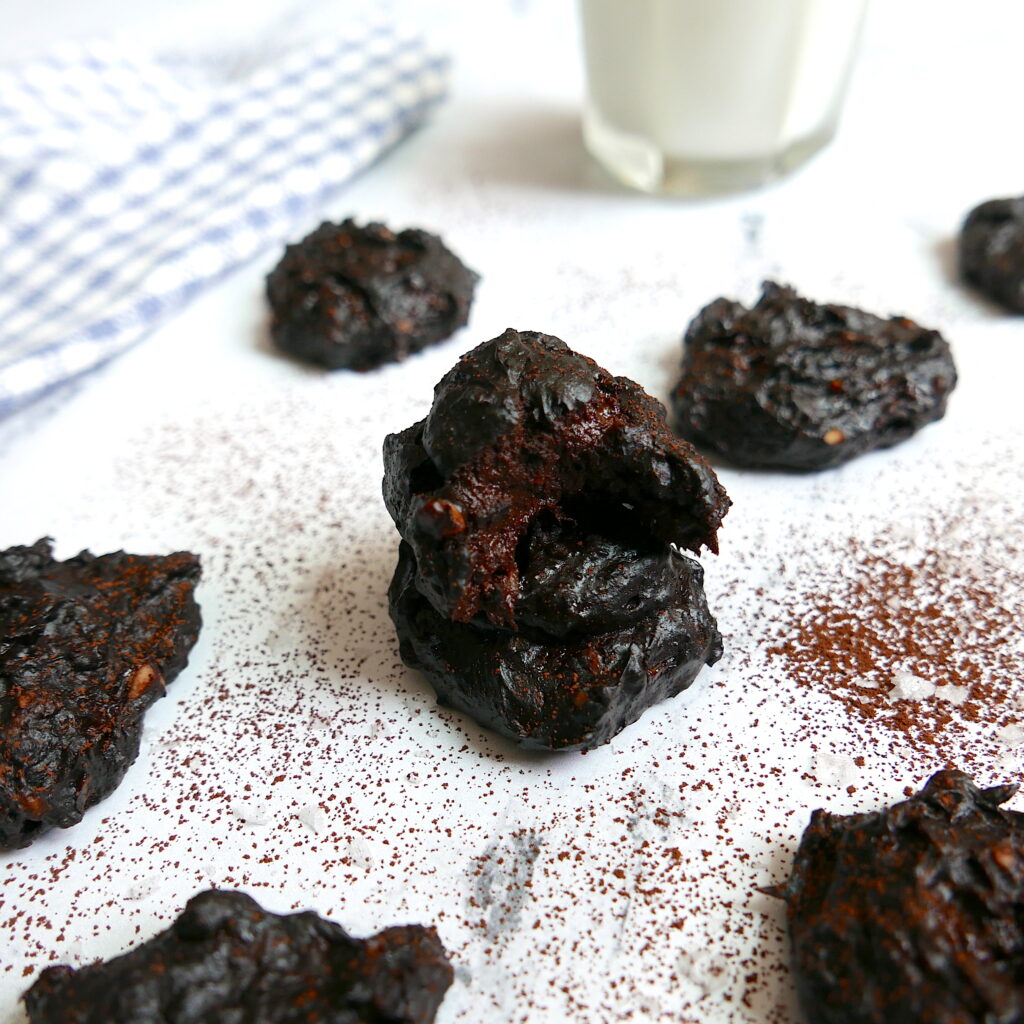 fudgy peanut butter cookies arranged in a pattern on a white counter with cocoa powder dusted around and a glass of milk in background