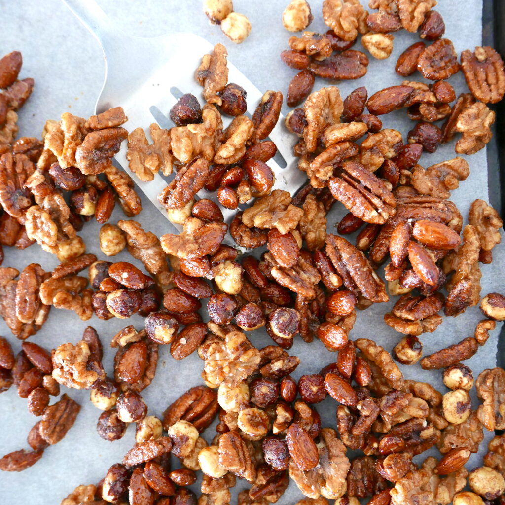 silver spatula scooping up spiced candied nuts from a baking sheet