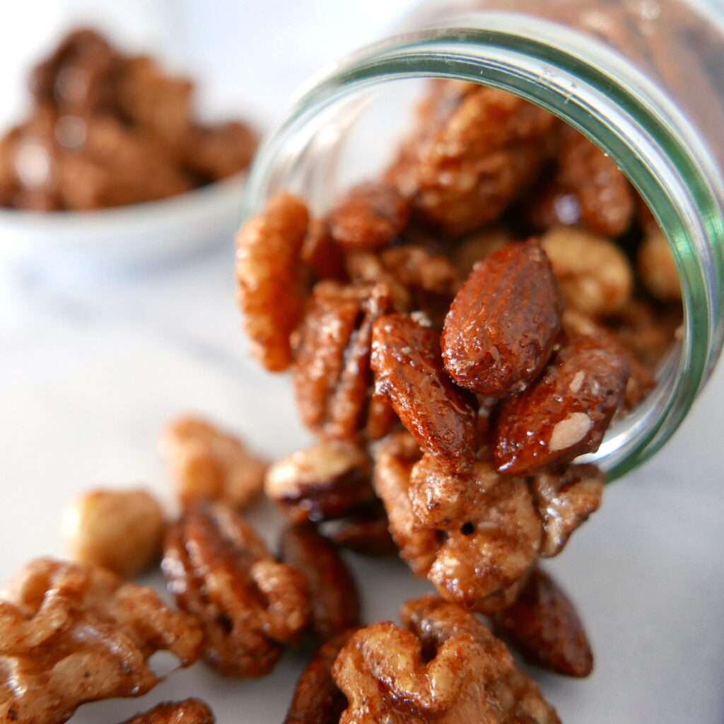 glass jar with mixed nuts spilling out of it onto a marble countertop