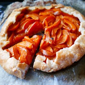 apricot gluten free galette on a baking sheet with one piece cut