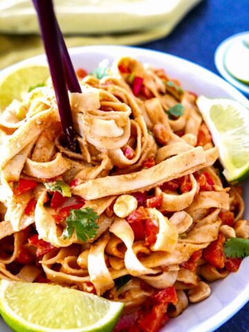 vegan peanut noodles on a white plate with chopsticks and pieces of lime