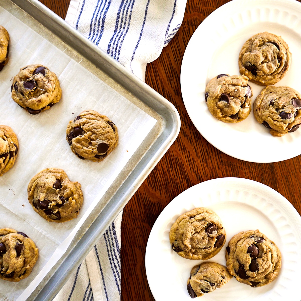 two plates of brown butter chocolate chip cookies with more cookies on a baking sheet