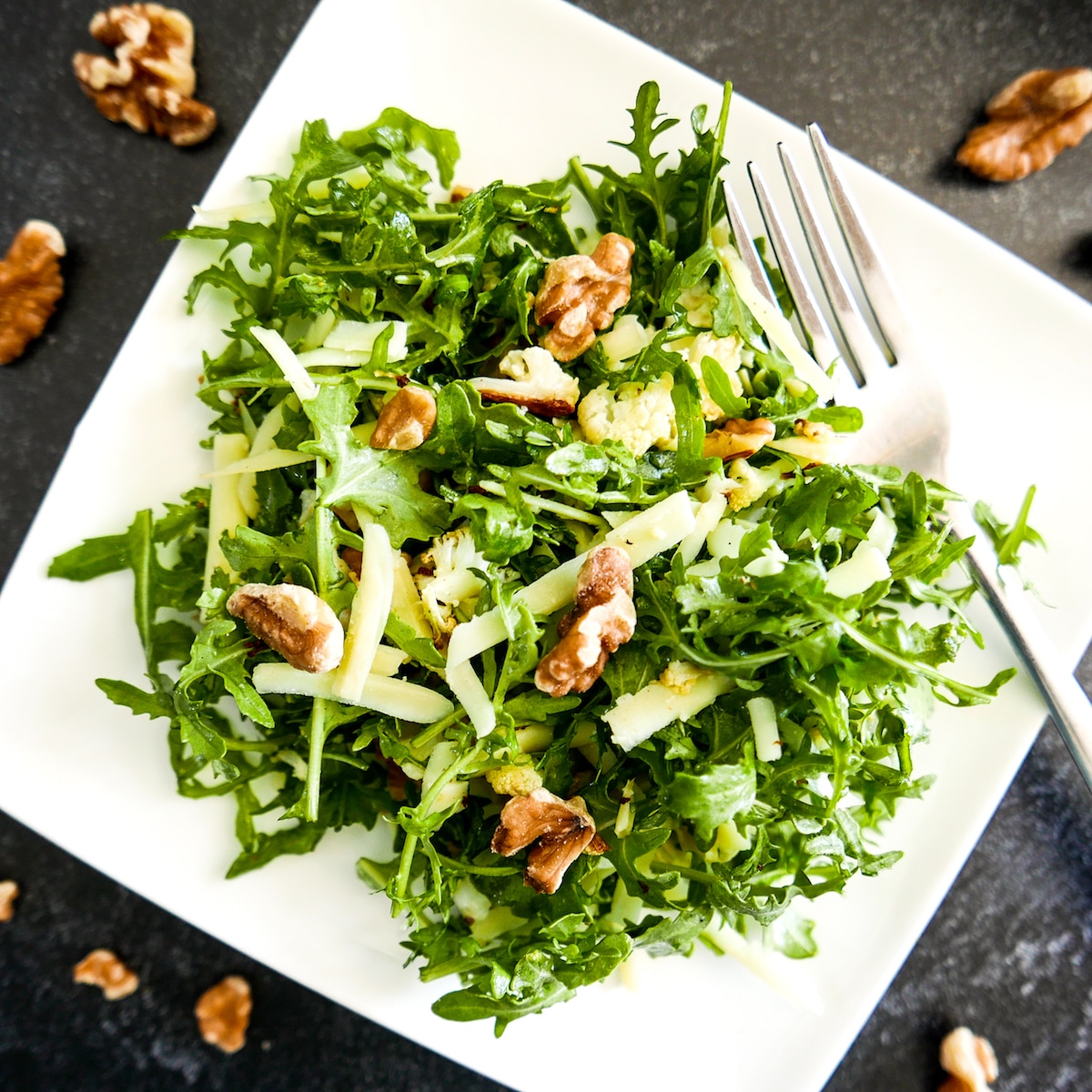 cauliflower salad with walnuts on a white plate with fork and walnuts scattered around.