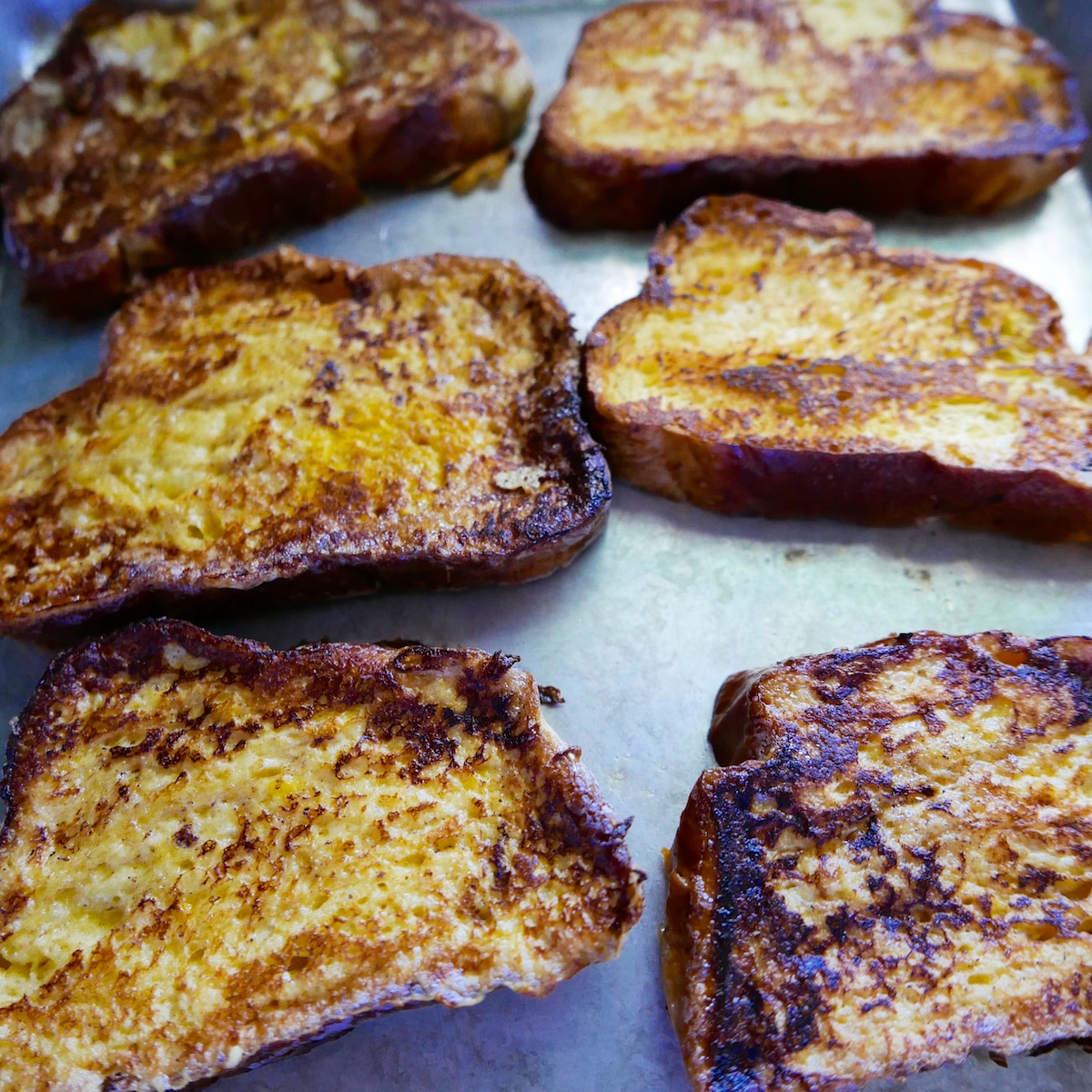Six pieces of cooked French toast resting on a baking sheet.