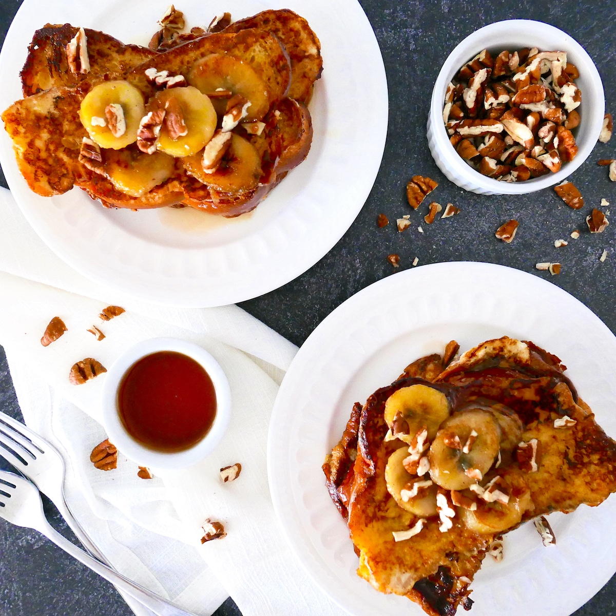 Two white places with french toast, caramelized bananas, pecans, and maple syrup.