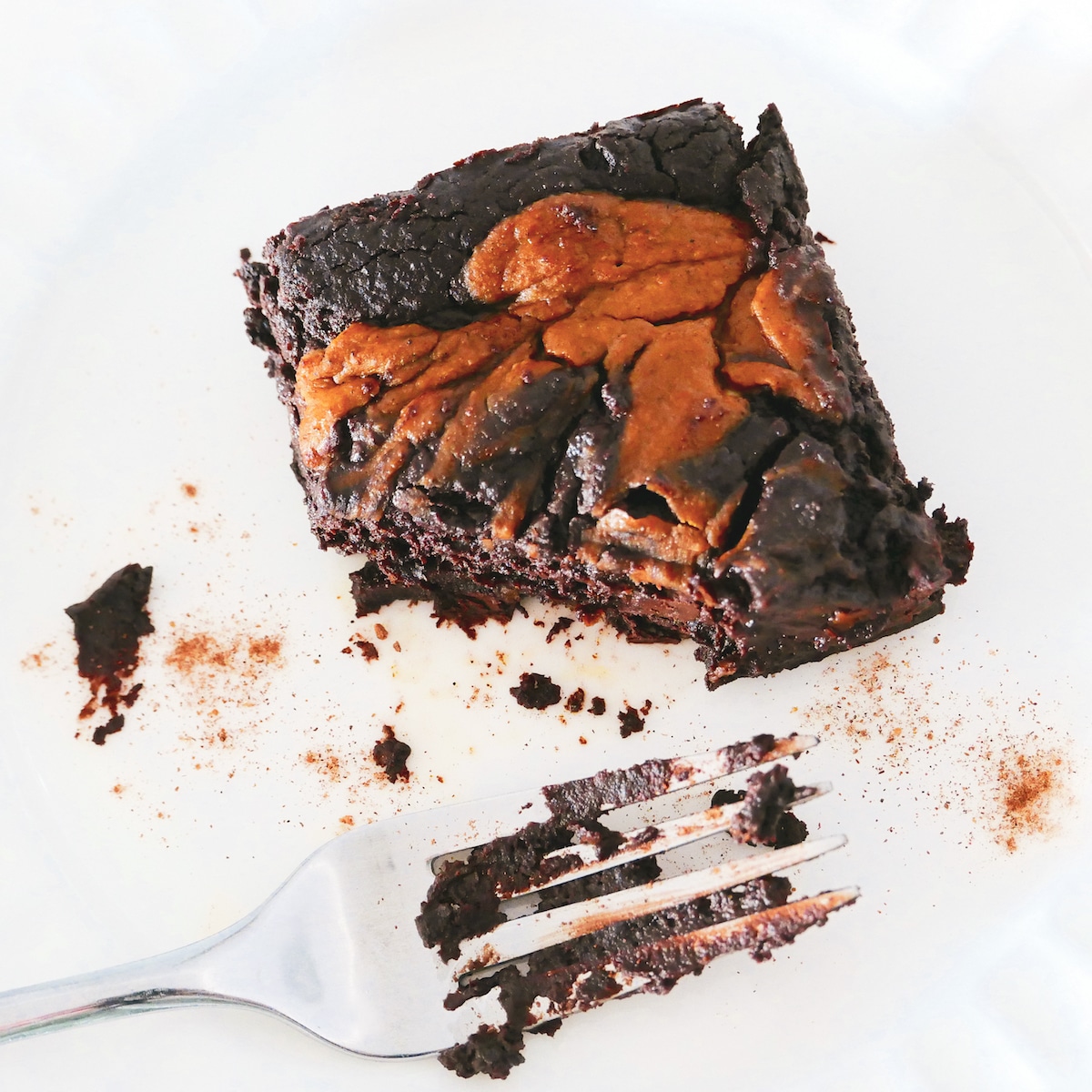 Chocolate pumpkin brownie cut with a fork and resting on a white plate.