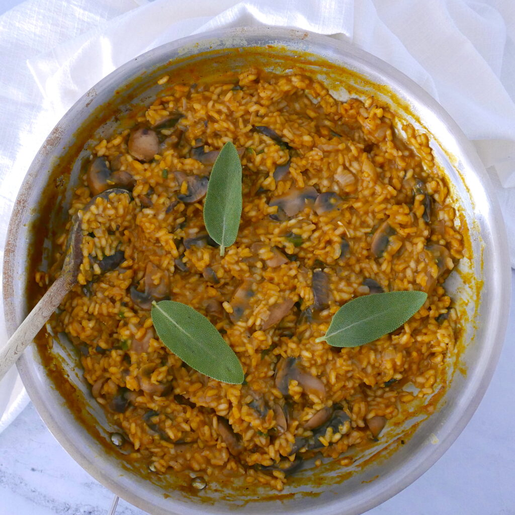 pumpkin and mushroom risotto in a skillet with wooden spoon and garnished with three sage leaves