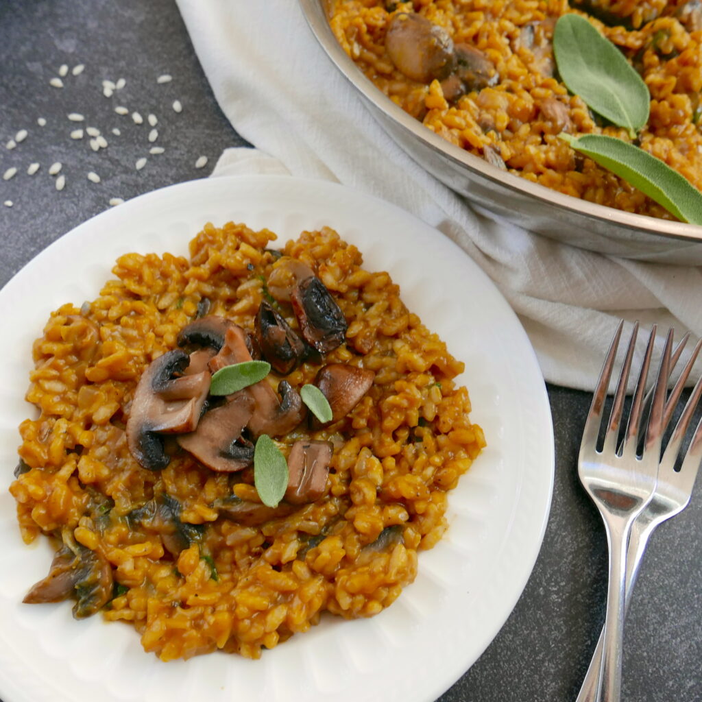 pumpkin risotto on a white plate with two forks and a pan of risotto in background