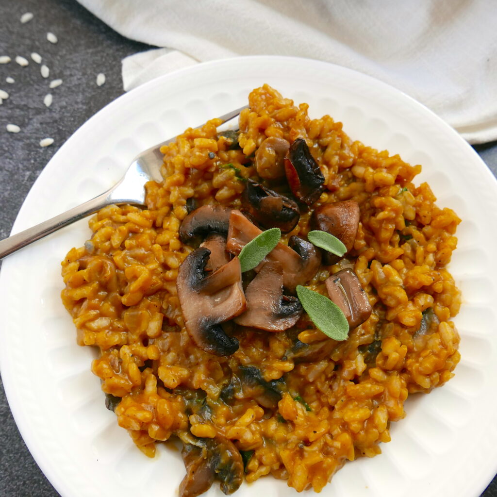 pumpkin and mushroom risotto garnished with mushrooms and sage on a white plate with fork and a white napkin in background