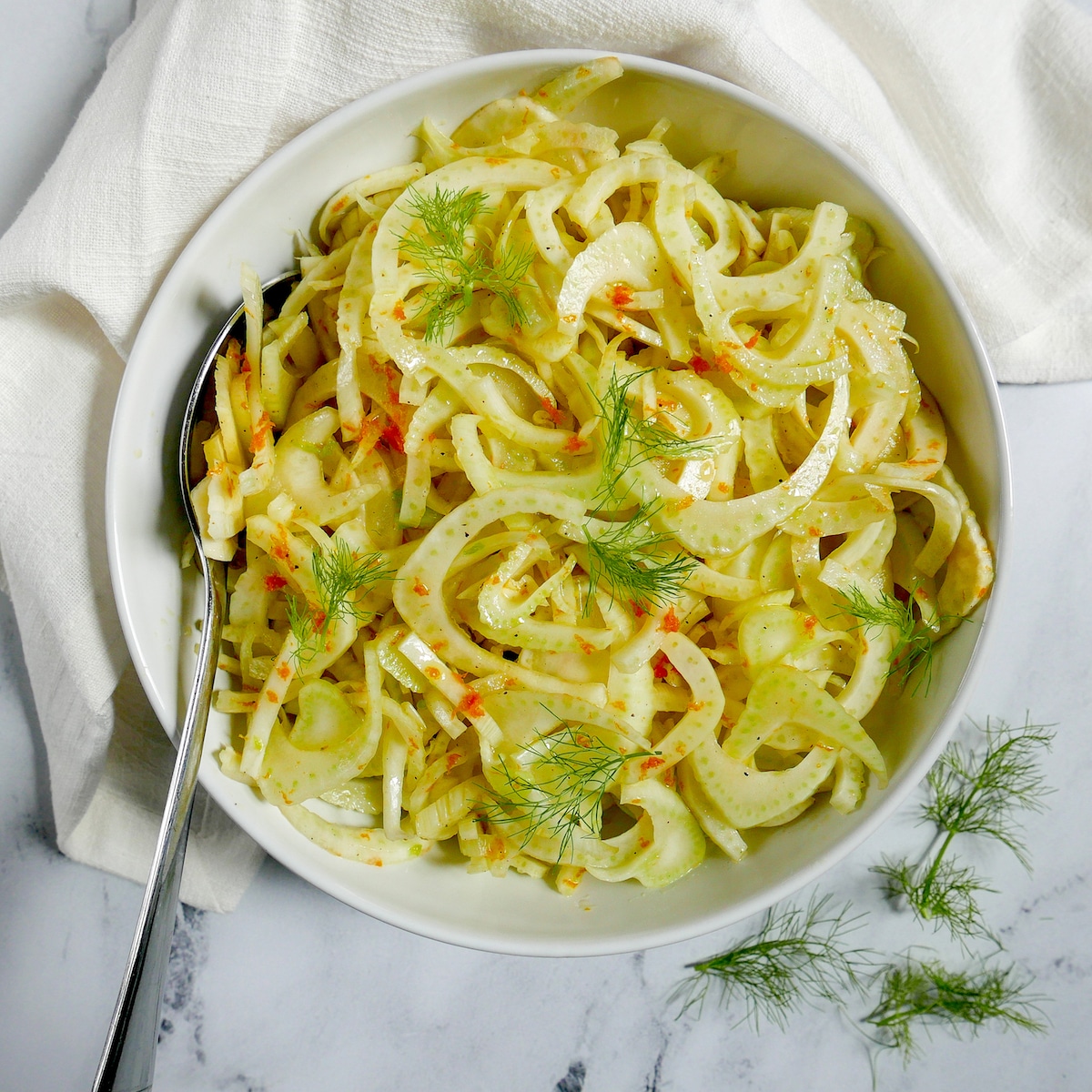 citrus fennel salad in a white bowl with a spoon and white napkin