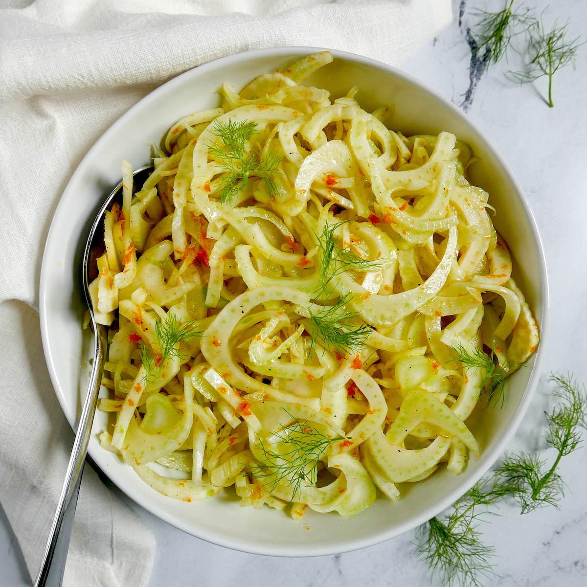 citrus fennel salad in a white bowl with a spoon and white napkin