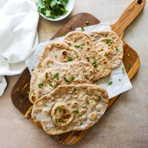 five pieces of sourdough naan arranged on a wooden cutting board with parchment paper.