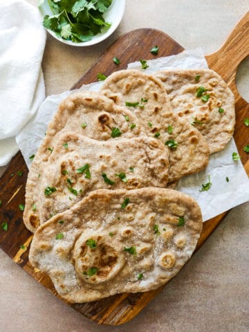 five pieces of sourdough naan arranged on a wooden cutting board with parchment paper.