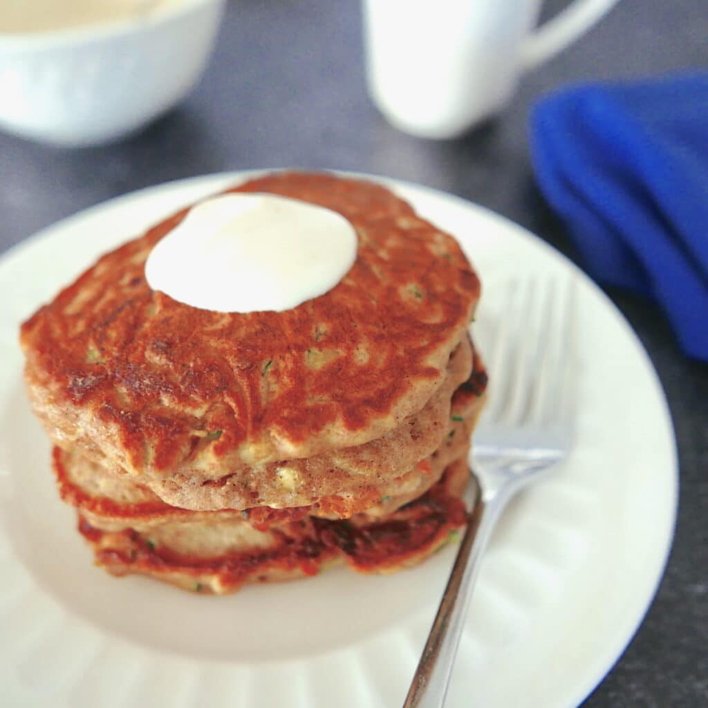 zucchini bread pancakes on a white plate with fork with white coffee cup in background
