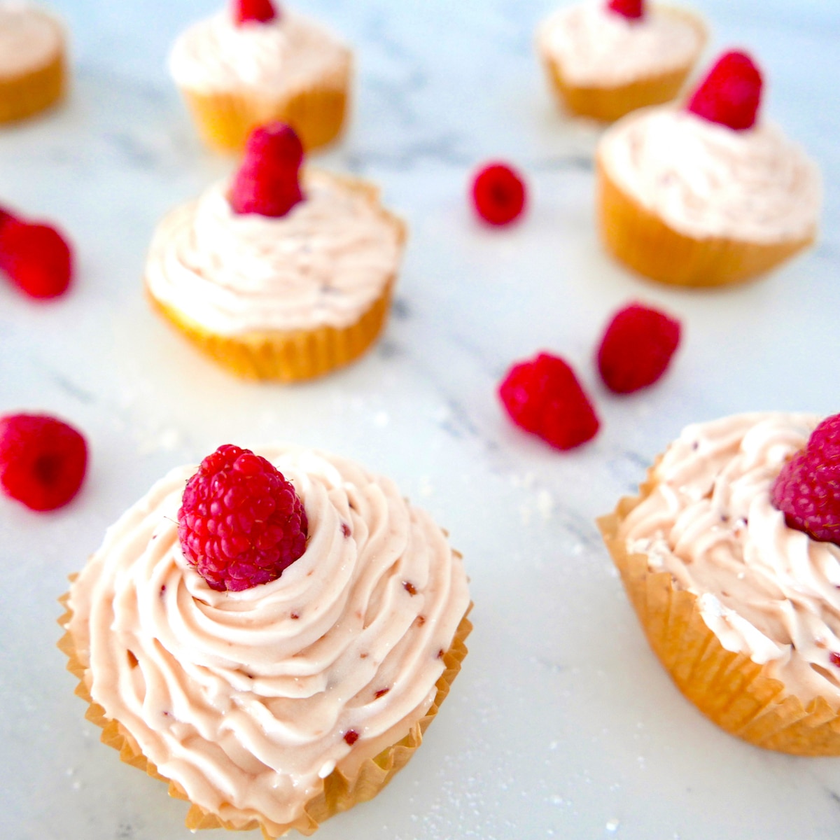 raspberry almond cupcakes arranged on a counter top with fresh raspberries.