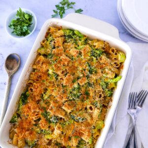broccoli pasta bake with plates, parsley, serving spoon, and napkin