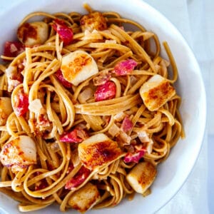 pasta with scallops and bacon in a white bowl.