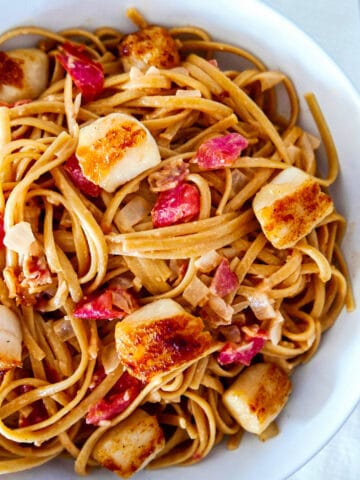 pasta with scallops and bacon in a white bowl.