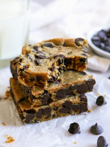 three vegan blondies stacked on parchment paper with chocolate chips scattered.