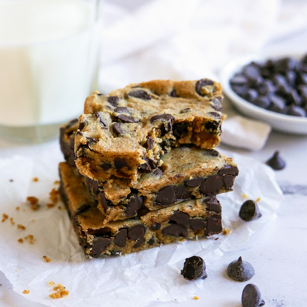 three blondies stacked on parchment paper with chocolate chips in background.