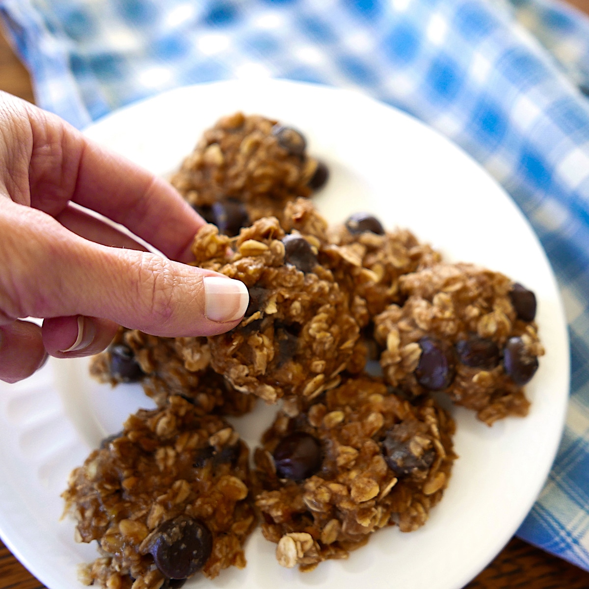 peanutbutter-banana-cookie.jpg peanut butter banana oatmeal cookies on a white plate with hand picking up one cookie