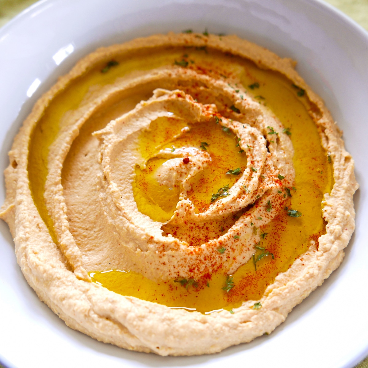 Paprika hummus in white bowl garnished with parsley.