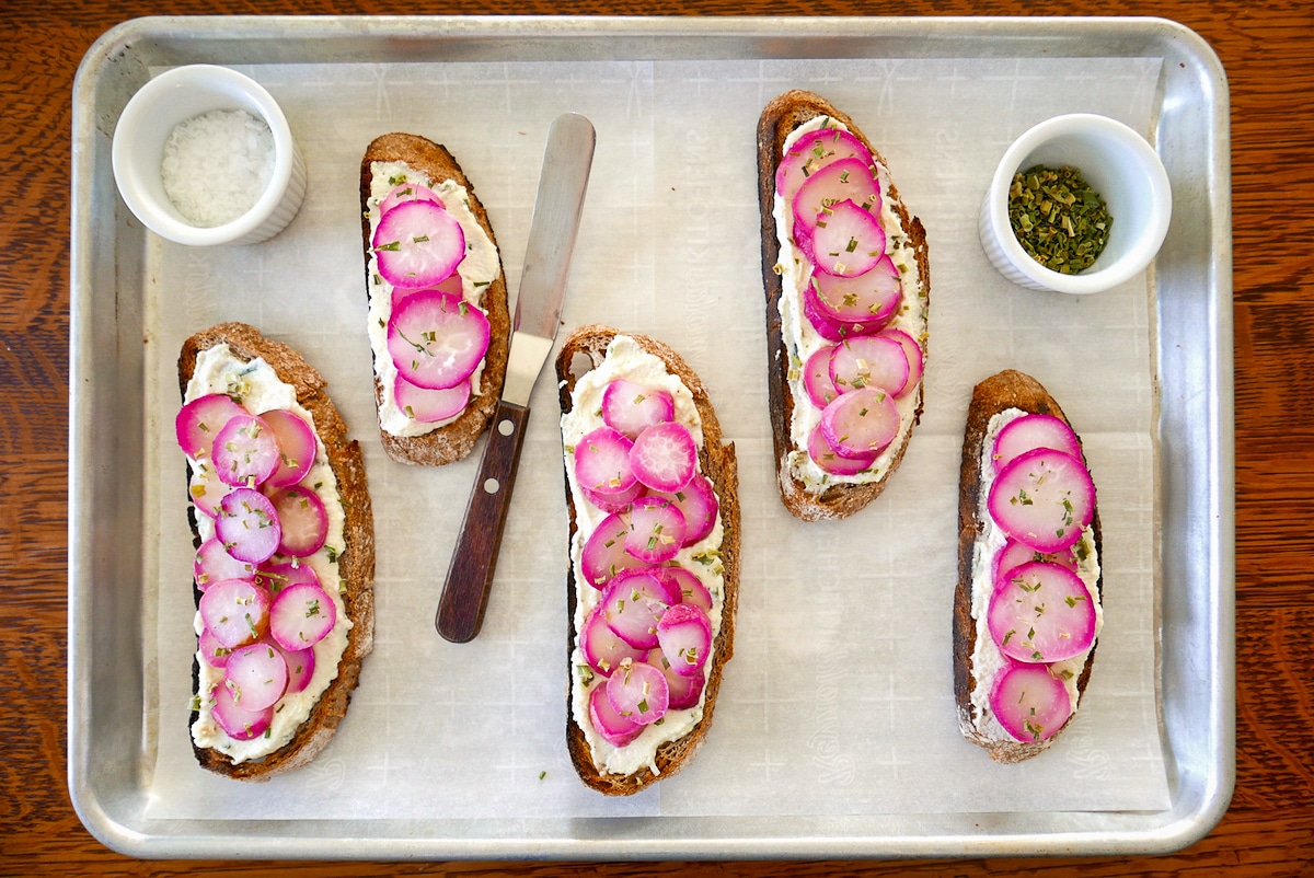 five pieces of radish toast on a baking sheet with condiments.