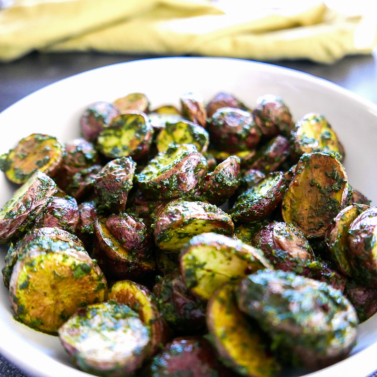 Roasted potatoes in a white bowl with a yellow napkin in the background.