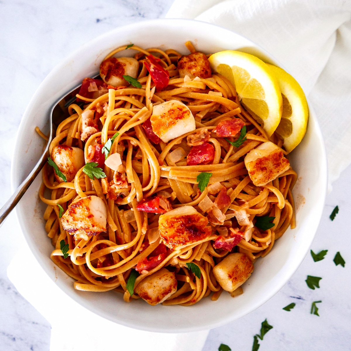 Rich and creamy pasta in a white bowl with lemon wedges and fork.