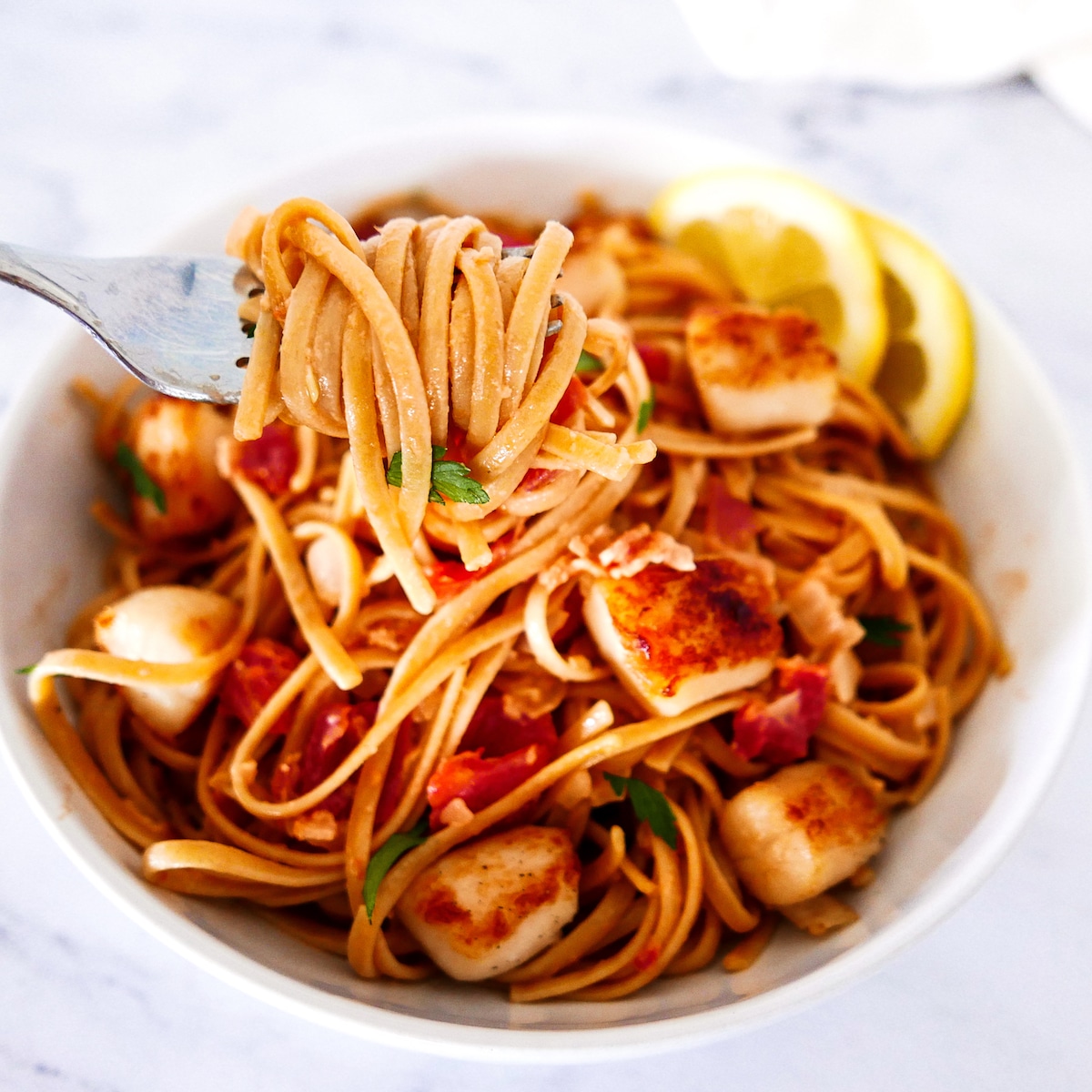 fork lifting up pasta from bowl with scallops and bacon.